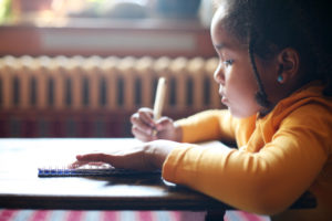Profile of little African girl writing in classroom.